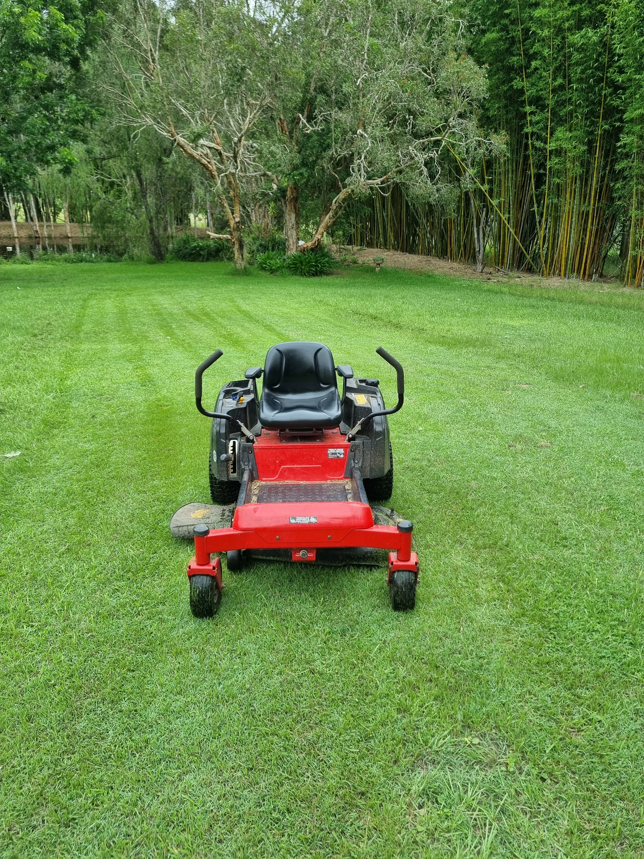 A zero-turn mower sitting on a freshly cut acreage lawn with clean stripes