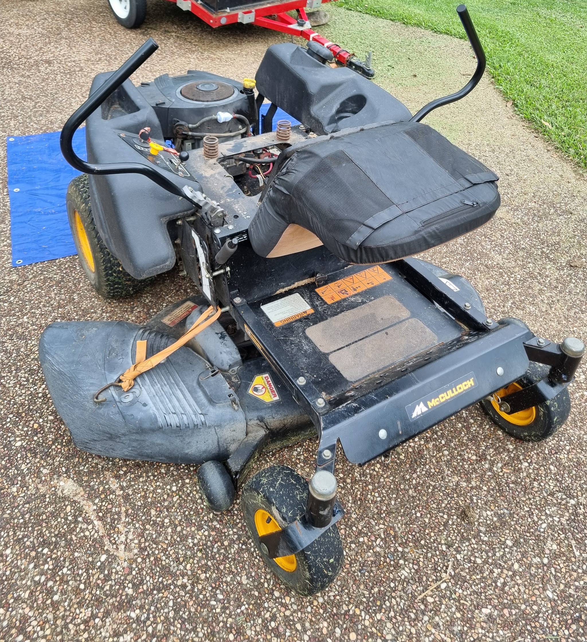 A zero-turn mower with the deck off on the driveway, trailer parked behind it